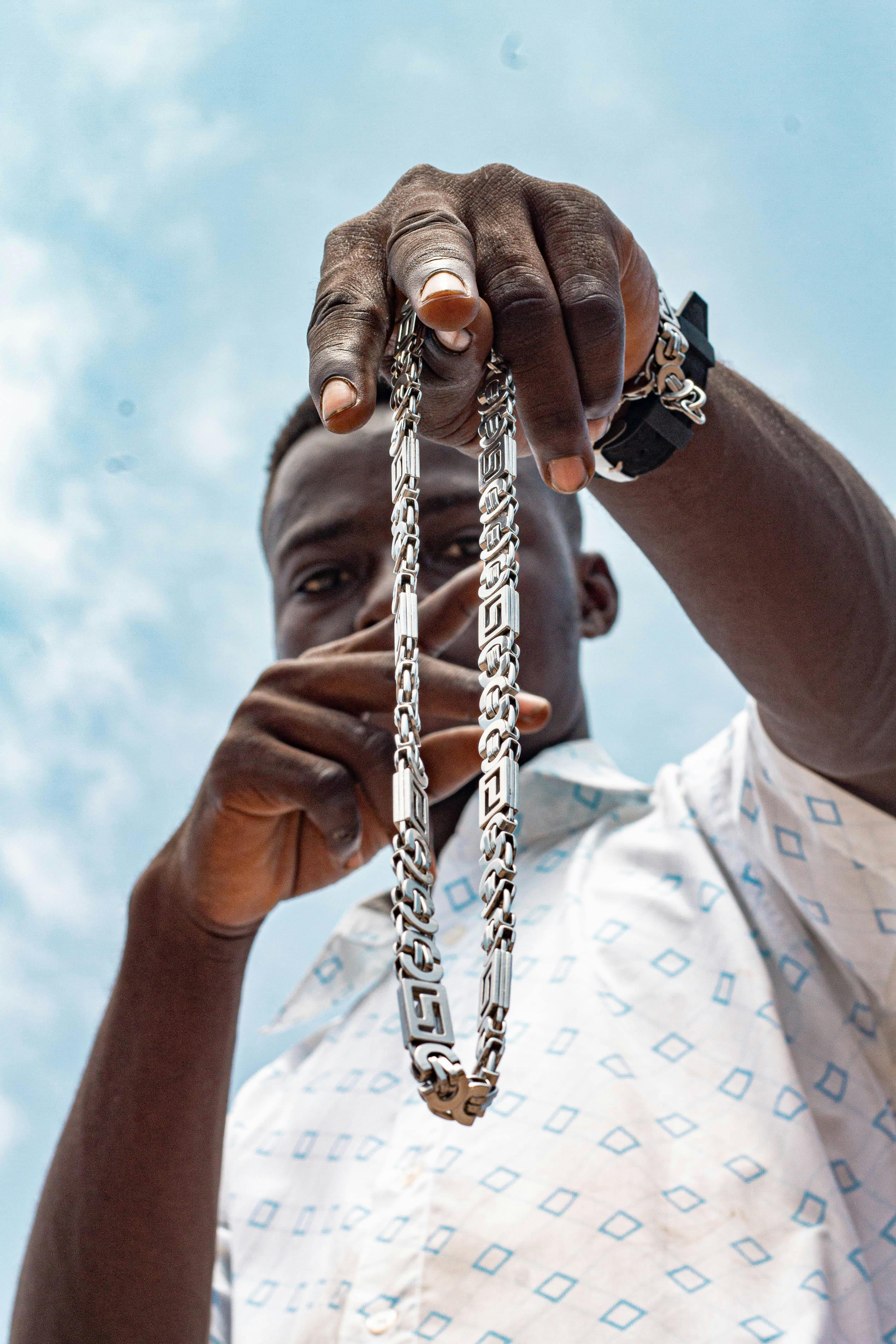 Low-angle shot of a man showcasing a silver necklace against a blue sky.