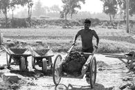 Grayscale Photo of Shirtless Man Pushing a Wheelbarrow