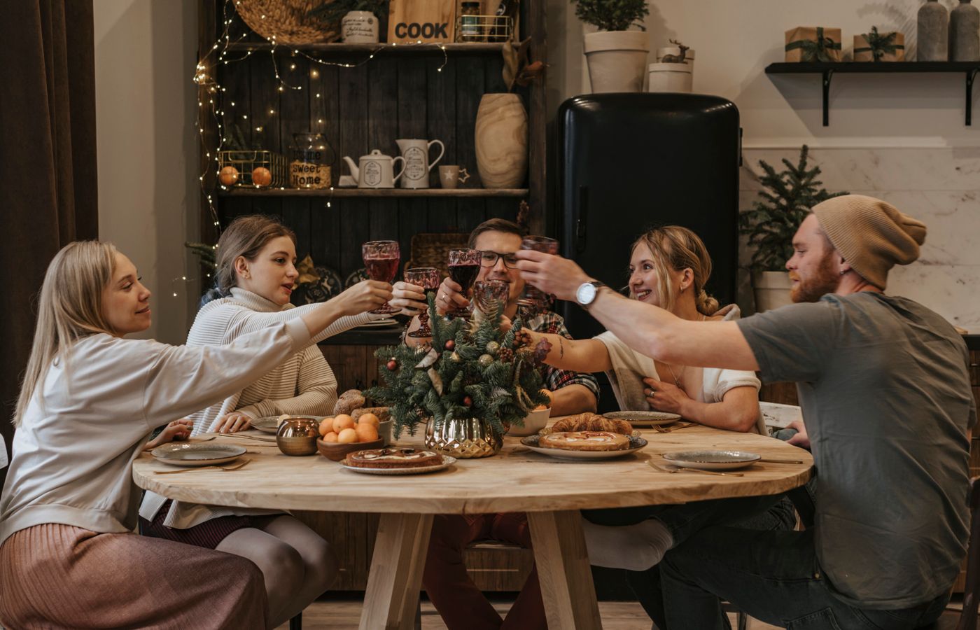 Warm indoor celebration with friends toasting around a decorated holiday dinner table.