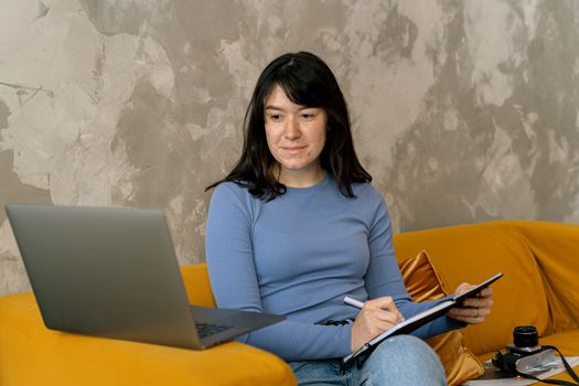 一名年轻女子在家舒适地工作，用笔记本电脑处理事务并做笔记