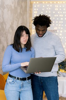 A young woman and man look at a laptop together in an indoor setting.
