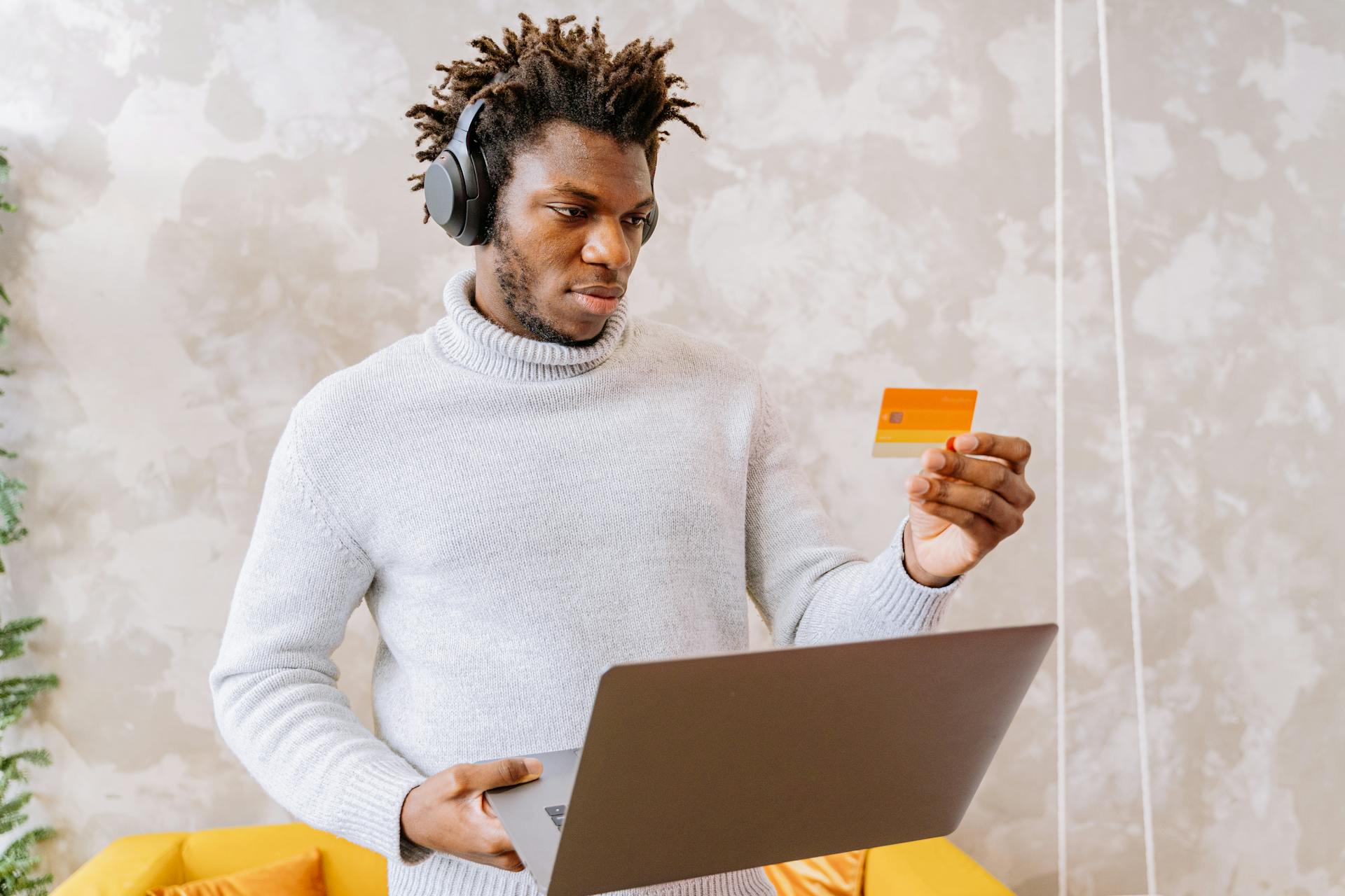 A man using a laptop and holding a credit card indoors, wearing a headset for online shopping.