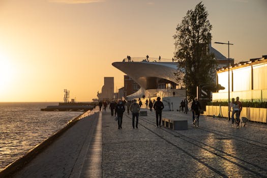 Golden hour view of people walking by the MAAT Museum at Lisbon waterfront, Portugal.