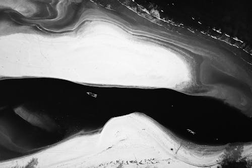 Black and white drone view of boats sailing on wavy ocean between sandy island shores