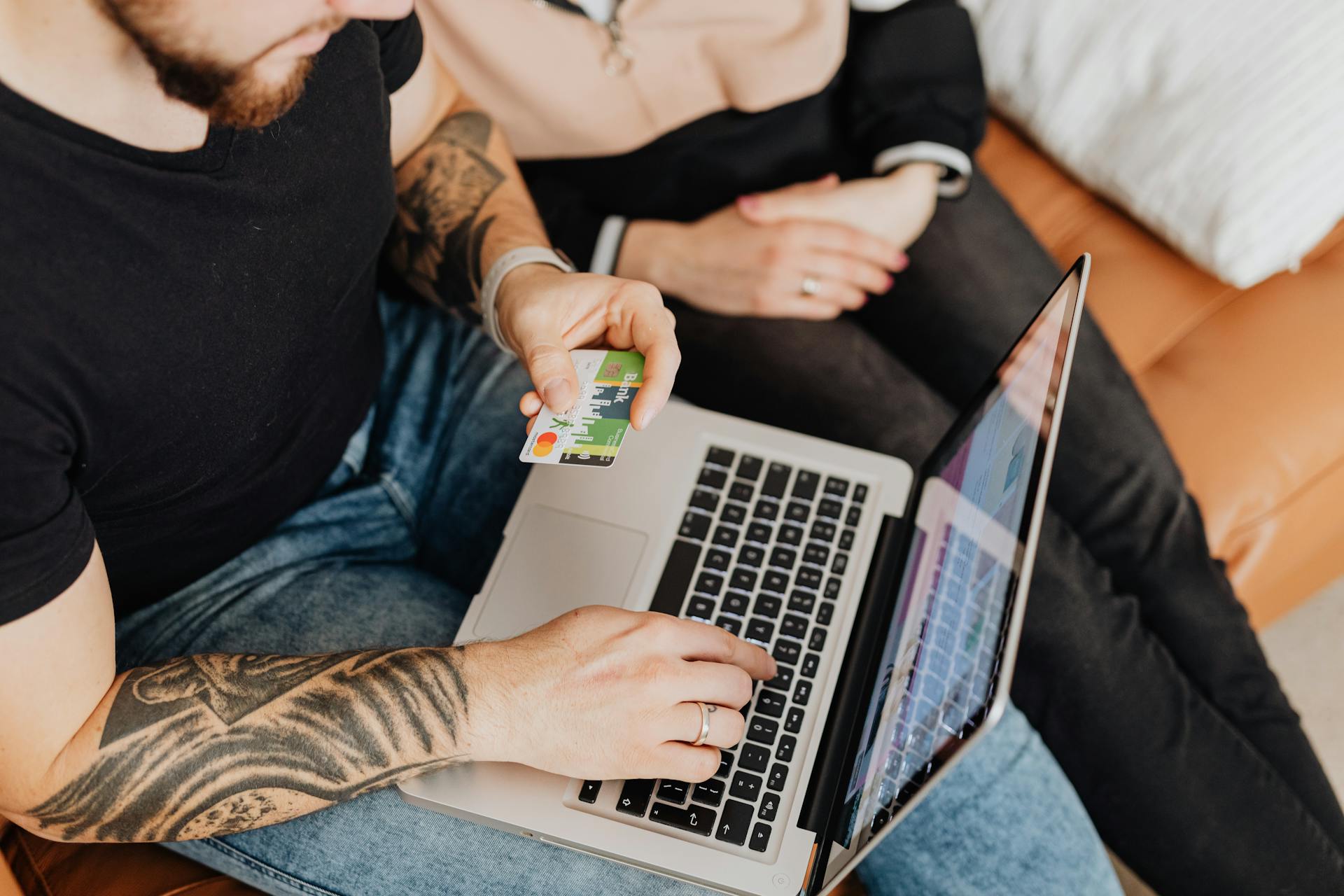 A couple casually shopping online using a laptop and credit card in a cozy indoor setting.