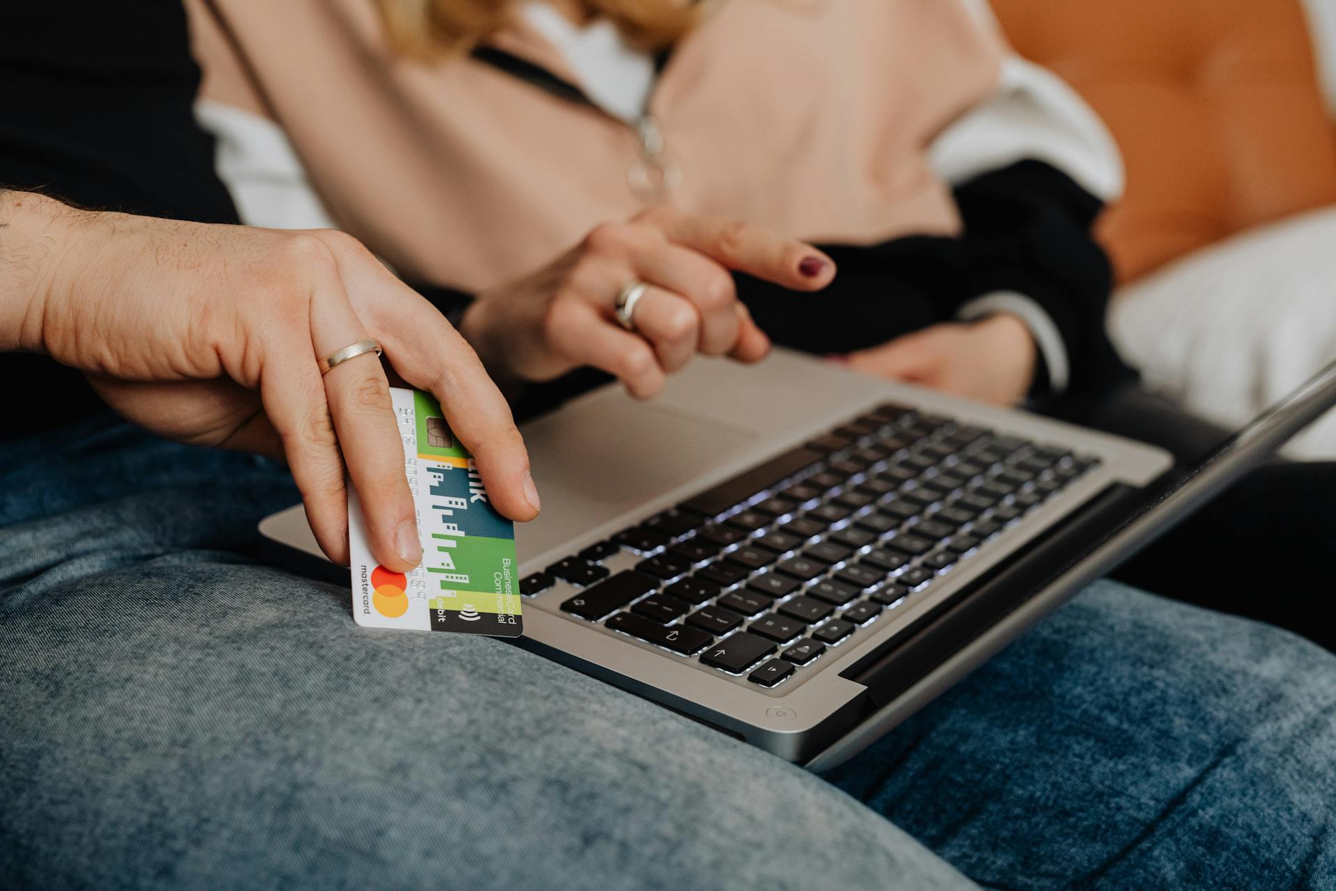 Two people shopping online with a credit card and laptop indoors.