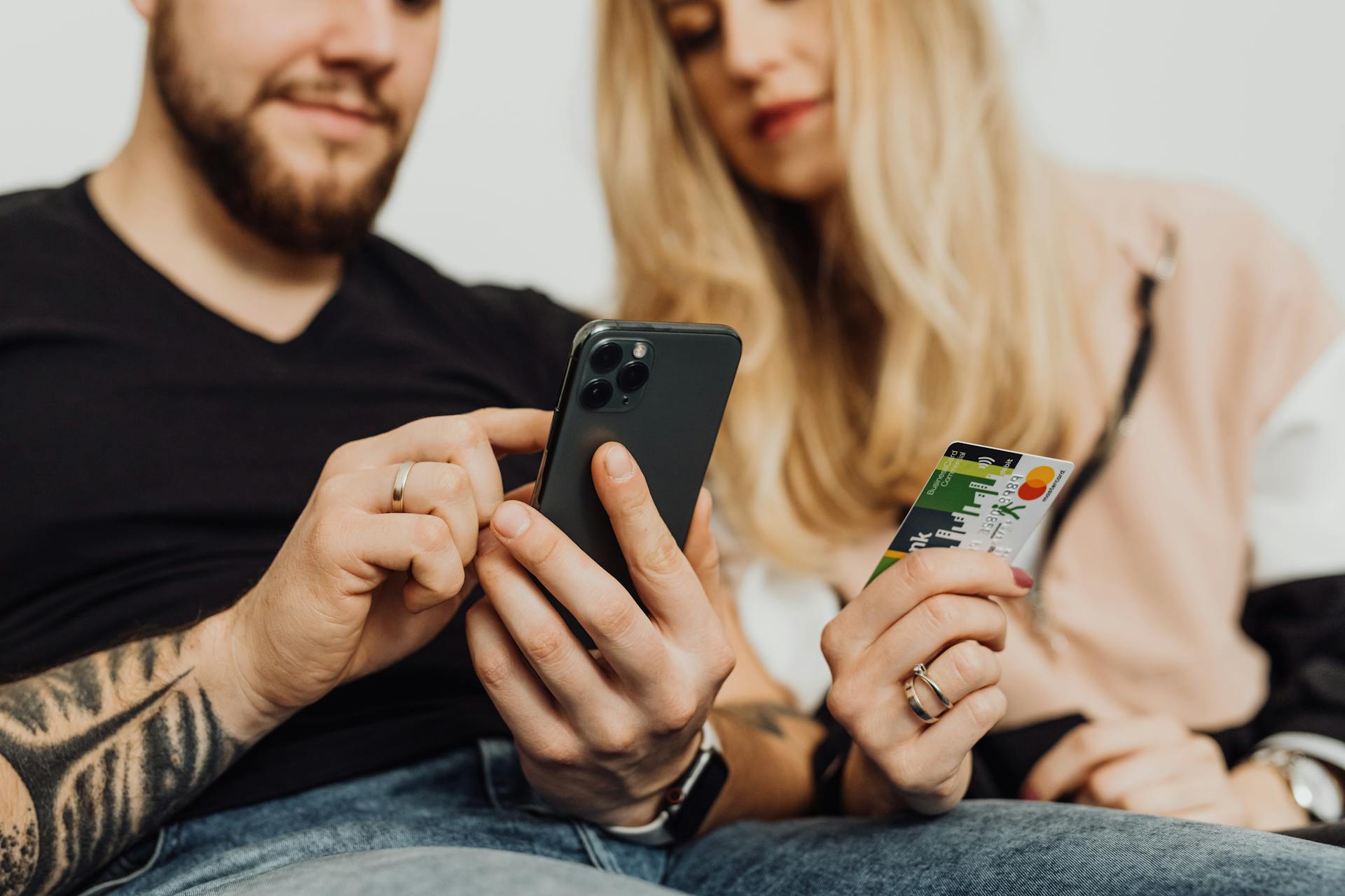 A couple using a smartphone and credit card for online shopping indoors.