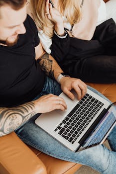 A tattooed man and a woman using a laptop together on a couch.