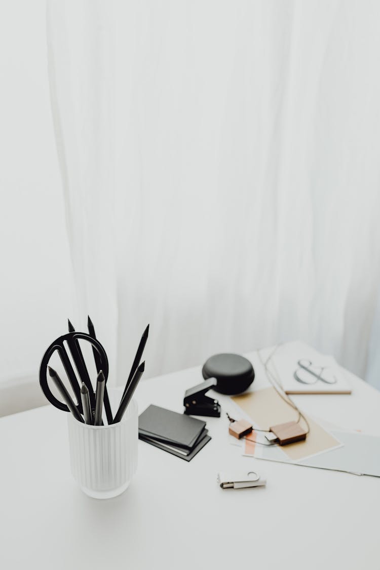 Pens In Cup And Flash Drive On White Desk