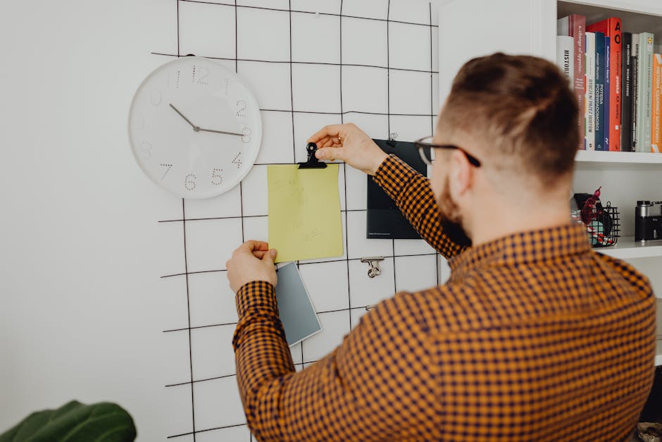 SoFi vs Marcus: Emergency Fund Growth Showdown Person arranging notes on an office wall grid beside a clock, creating an organized workspace.