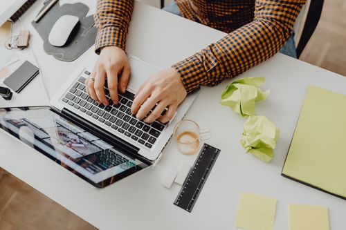 Free Overhead view of a person typing on a laptop in an office setting with crumpled papers and stationery. Stock Photo