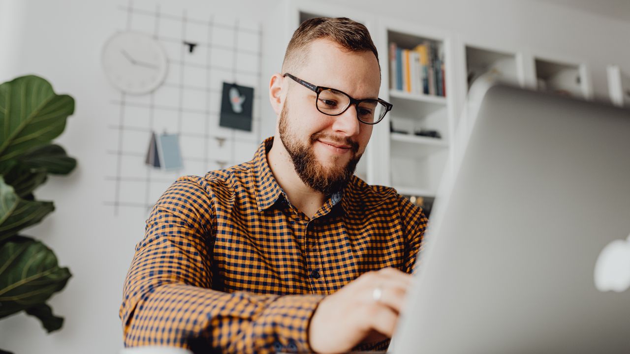 A confident man with glasses working on a laptop in a modern office setting.