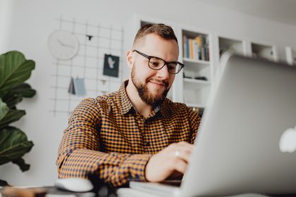 A confident man with glasses working on a laptop in a modern office setting — photo by Kaboompics on Pexels