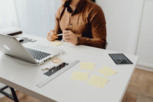 Modern workspace setup with laptop, office supplies, and a person in a checked shirt.