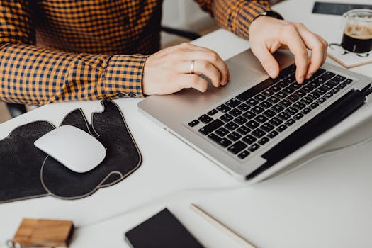 Focused shot of hands typing on a laptop with coffee and accessories nearby.