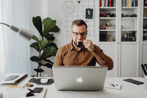 Free A Man Drinking Coffee while Using Laptop Stock Photo