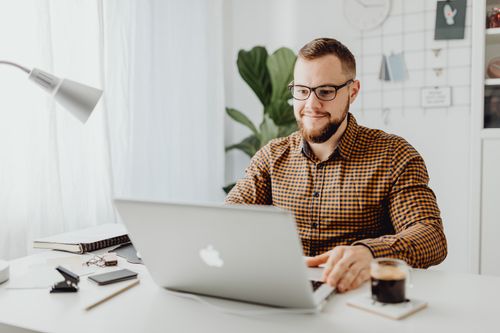Free Adult man with eyeglasses typing on a laptop in a modern home office setting. Stock Photo