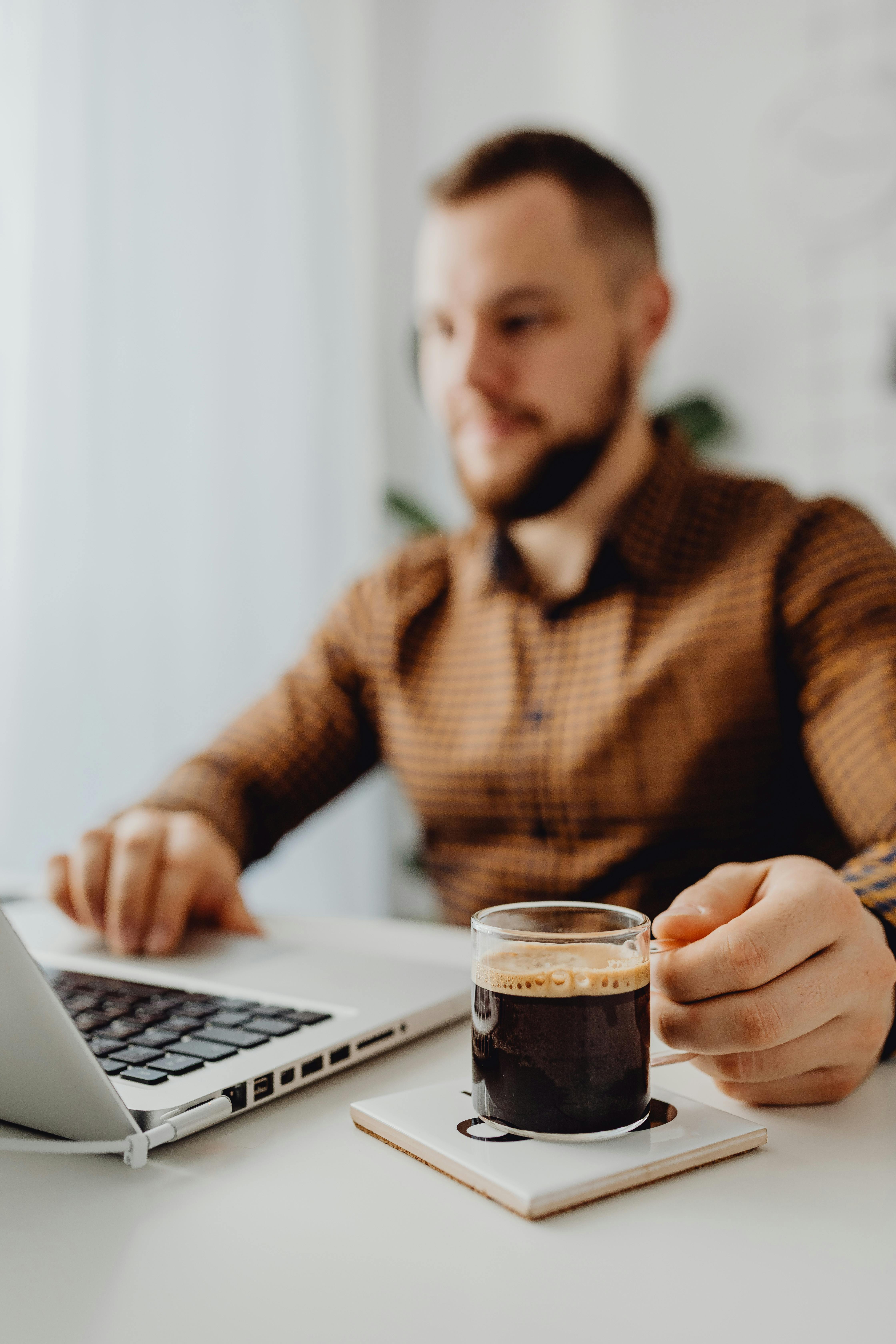 一名男子在家庭办公室里端着咖啡杯使用笔记本电脑