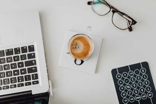 Top view of a modern workspace featuring a laptop, eyeglasses, coffee cup, and calculator on a desk.