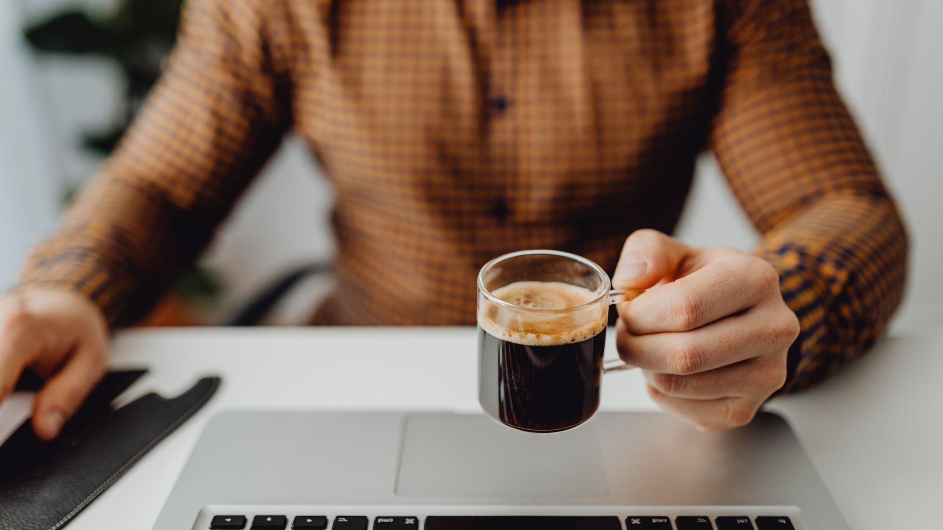 Modafinil vs Caffeine: Comparing the Effects Adult man in checkered shirt holding espresso cup while working on laptop in office setting — modafinil vs caffeine