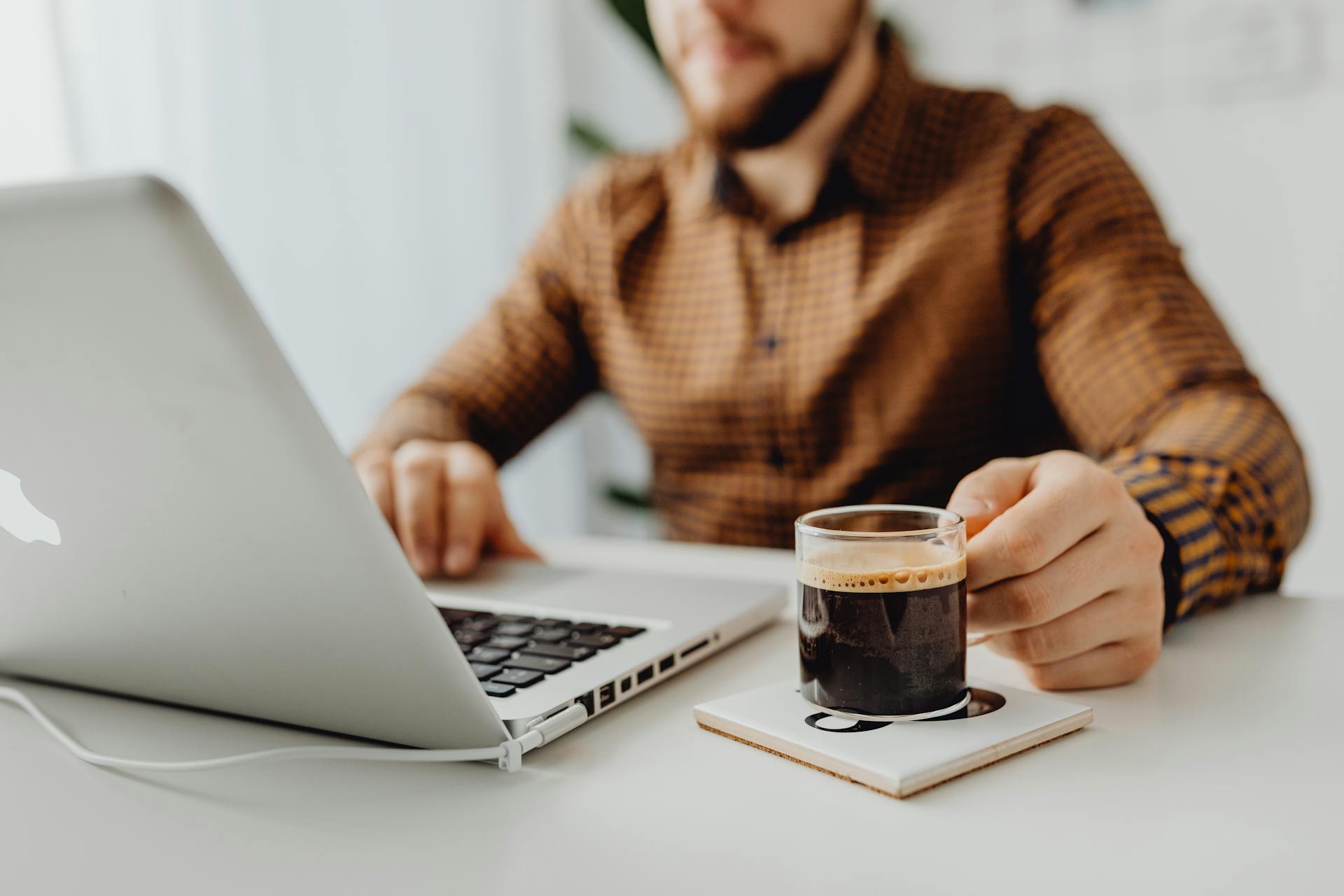 Free Man in Brown Dress Shirt Sitting at the Table With Macbook Pro Stock Photo