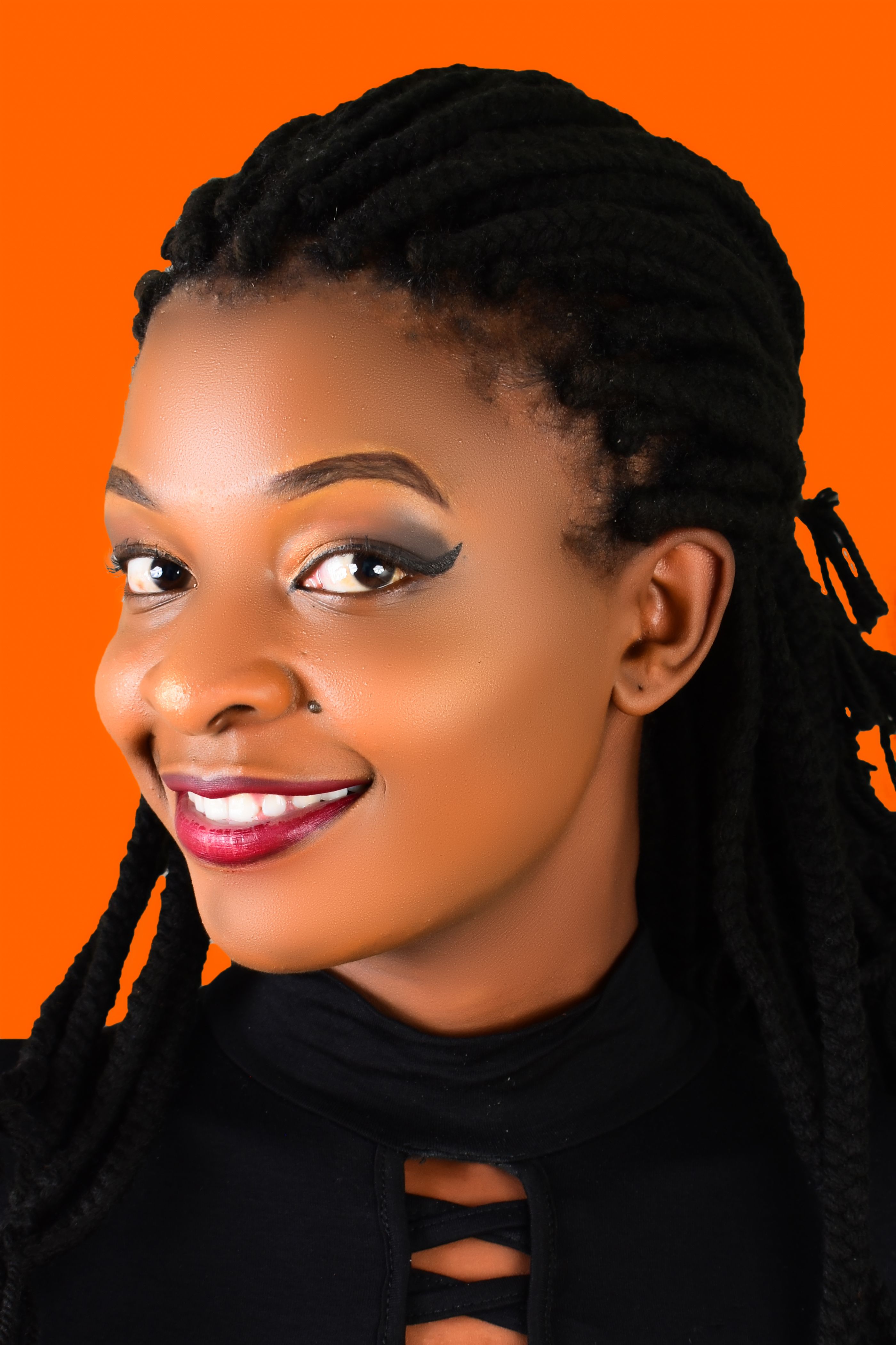 Vibrant portrait of a smiling woman with braided hair against an orange background.