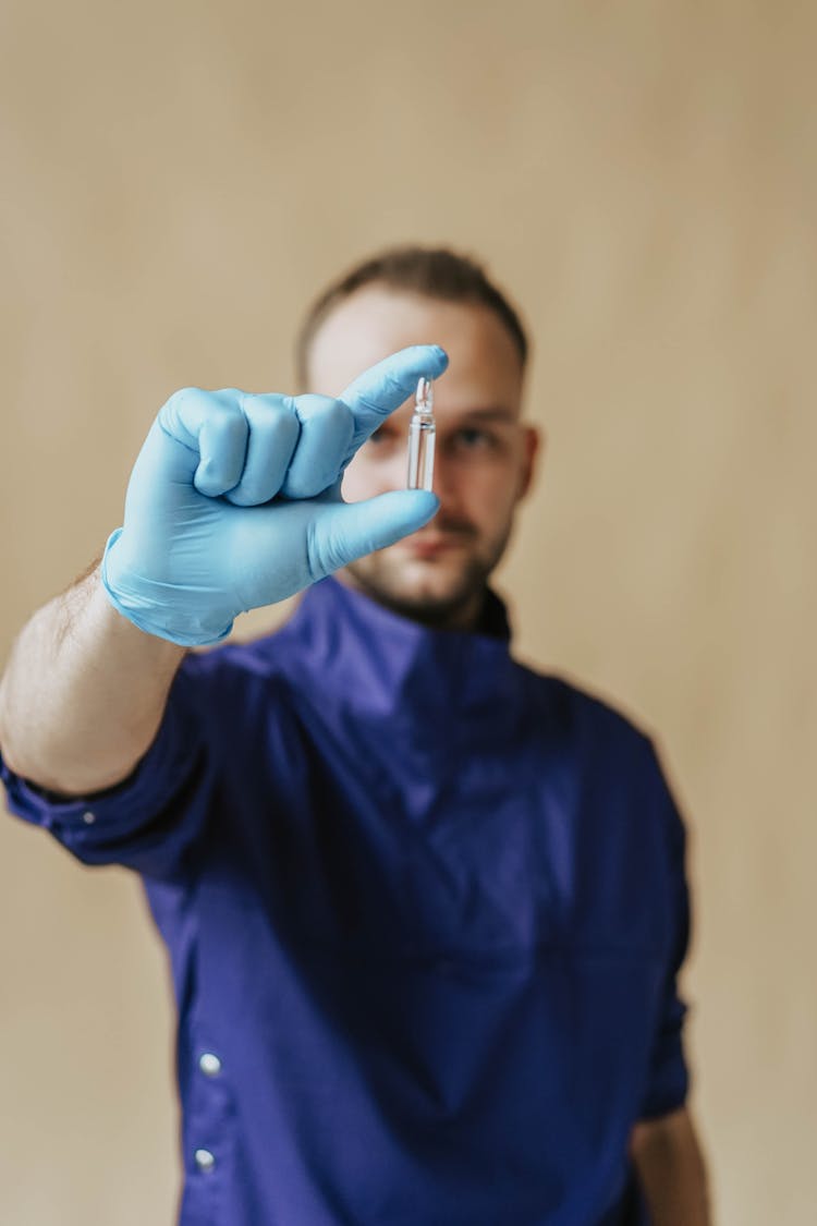 A Man In Blue Scrub Suit Holding A Small Glass Bottle