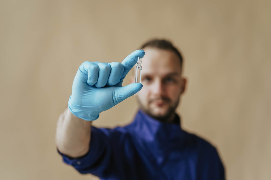 A Man in Blue Scrub Suit Holding a Small Glass Bottle