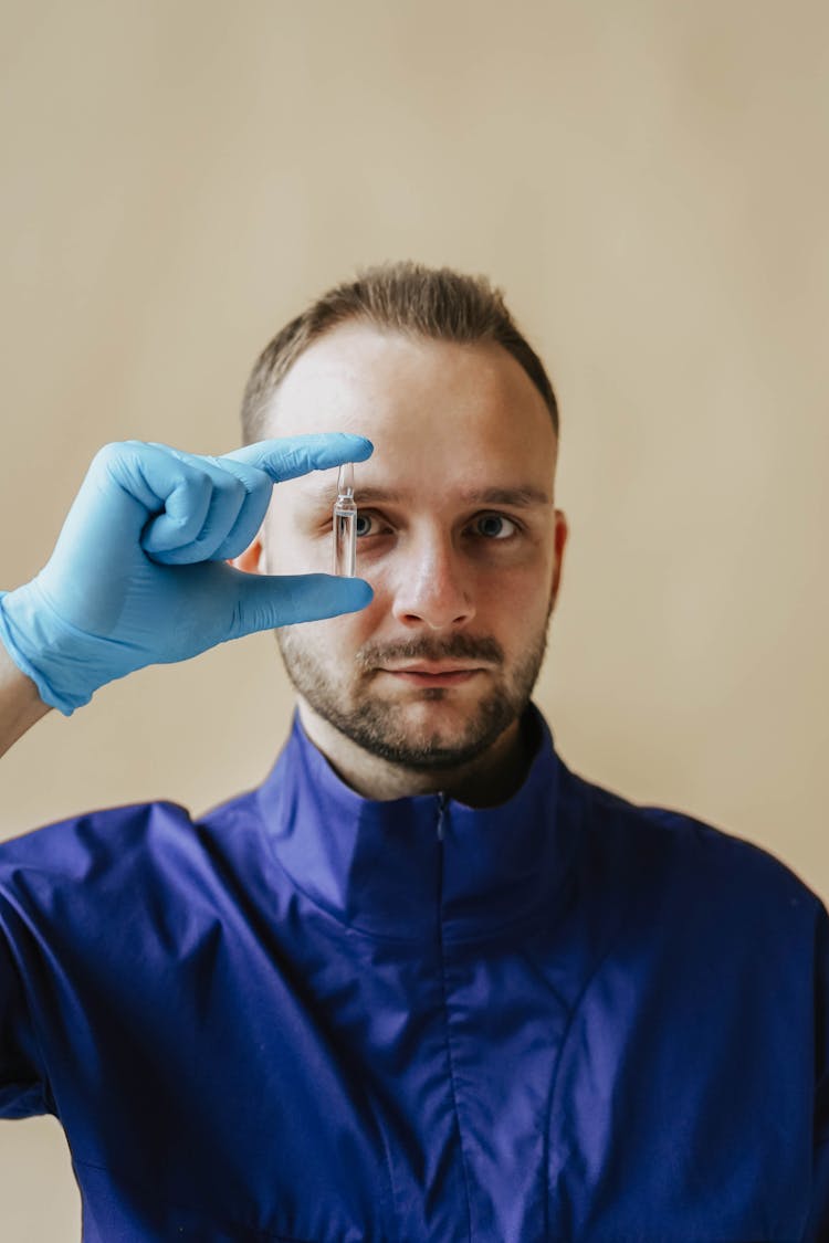 A Man In Blue Scrub Suit Holding A Small Glass Bottle