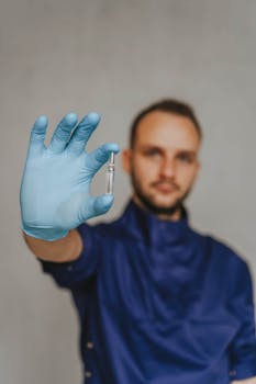 Blurred healthcare professional presenting small vial with focus on gloved hand.