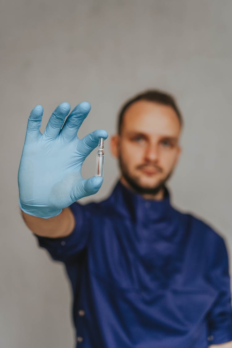 A Man In Blue Scrub Suit Holding A Small Glass Bottle