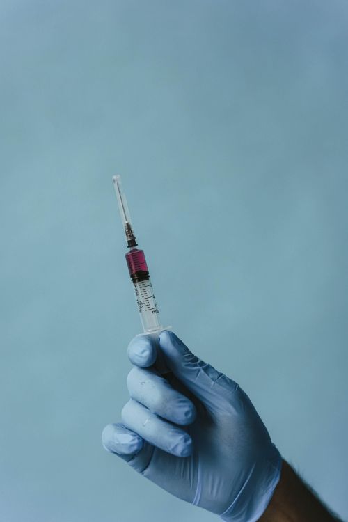 Free A gloved hand holding a syringe against a plain background, medical setting. Stock Photo