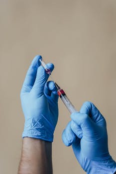 Close-up of gloved hands preparing a syringe with a vaccine indoors.