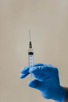 特写镜头中，一只戴着手套、拿着注射器的手置于朴素的背景上