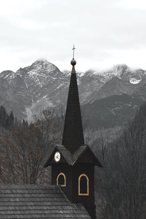 Black and White Church Near Brown Bare Trees and Snow Covered Mountain