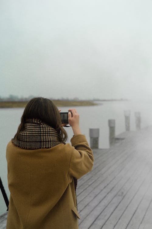 Free Woman in Coat Taking a Picture Using Her Camera Stock Photo