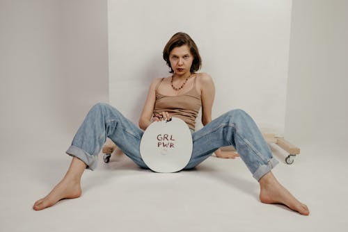 Confident young woman sitting with spread legs and showing banner with Grl Pwr inscription