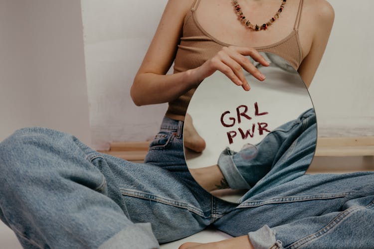 Woman In Brown Tank Top And Blue Denim Jeans Holding Round Mirror