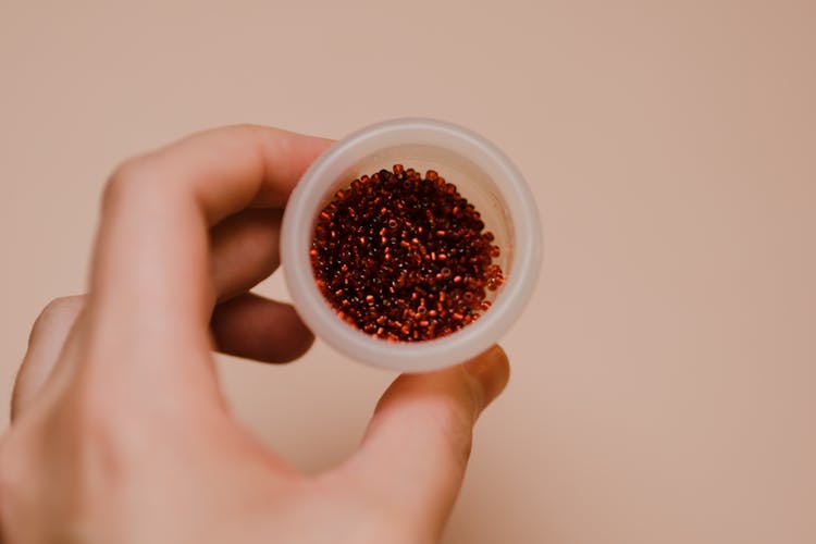 Hand Holding Clear Round Container With Red Beads