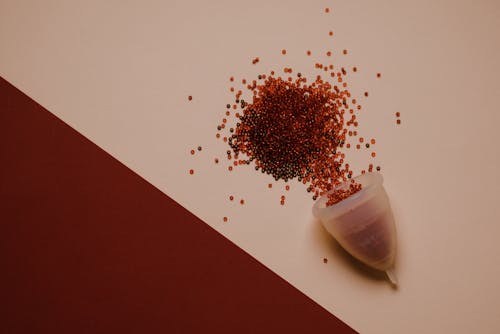 Top view of silicone menstrual cup with red beads scattered on pink surface