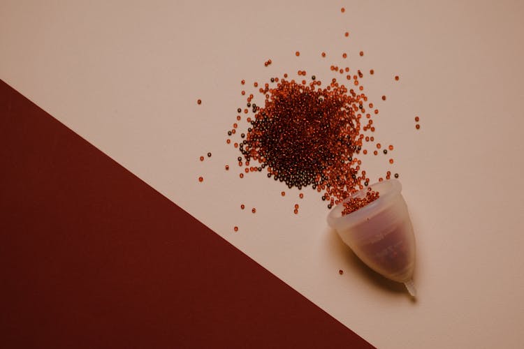 Menstrual Cup With Red Beads Scattered On Desk