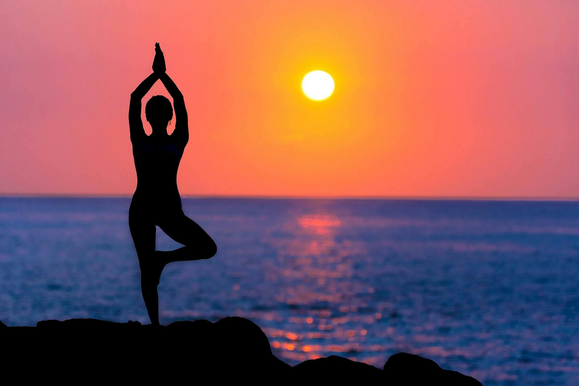 A photo of a CBD user practicing yoga by herself on a serene beach at sunset.