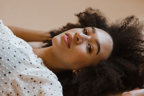 Free Elegant portrait of a woman with natural curly hair, lying down in a polka dot dress. Stock Photo