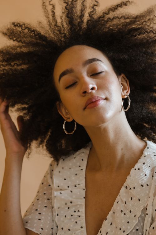 Free Chic studio portrait of a woman with afro hair and hoop earrings in a polka dot dress. Stock Photo