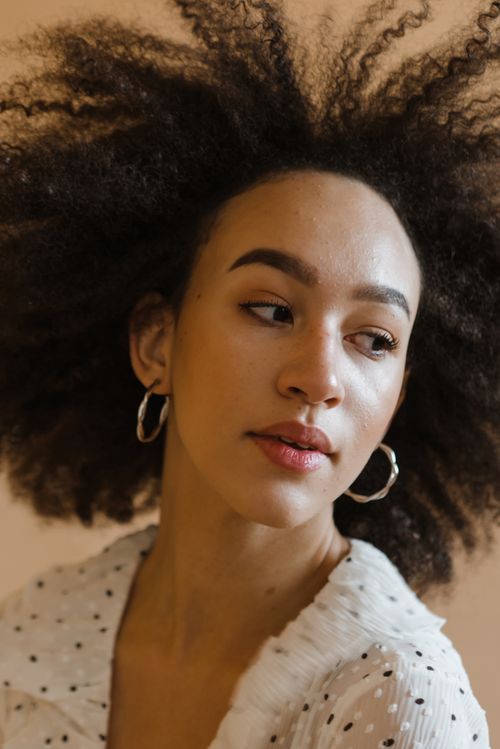 Free Stylish portrait of a young woman with afro hair and hoop earrings in a studio setting. Stock Photo