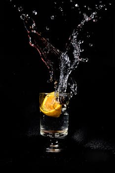 Dynamic splash of liquid with lemon in a glass on a black background.