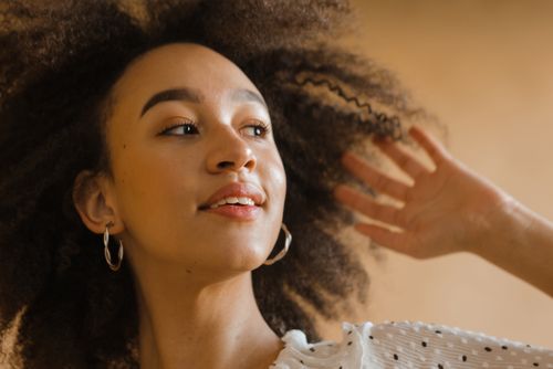 Free Close-up of a smiling woman with curly hair, wearing earrings, in a soft indoor setting. Stock Photo