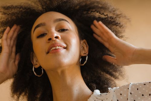 Free Portrait of a confident woman with curly hair, wearing hoop earrings and a polka dot top. Stock Photo