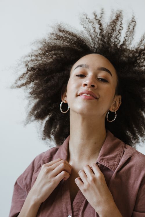 Free Portrait of a young woman with afro hair and hoop earrings, posing confidently in a studio setting. Stock Photo