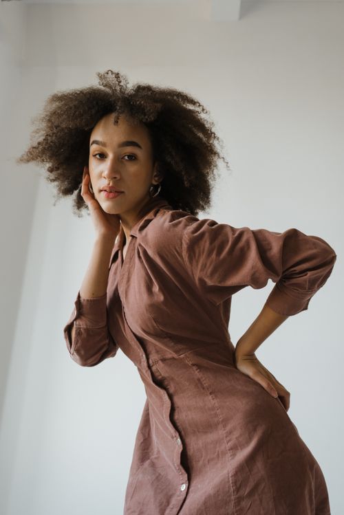 Free Stylish portrait of a young woman with afro hair posing naturally indoors in a brown dress. Stock Photo
